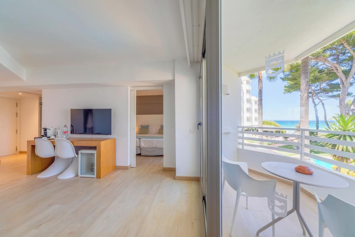 A modern hotel room with a balcony, a dining area, and a TV.