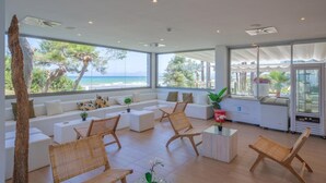 A spacious living area with a large window overlooking the beach, a seating area with white sofas and wicker chairs, and a small table with a plant. - Playa Esperanza Resort (Muro)