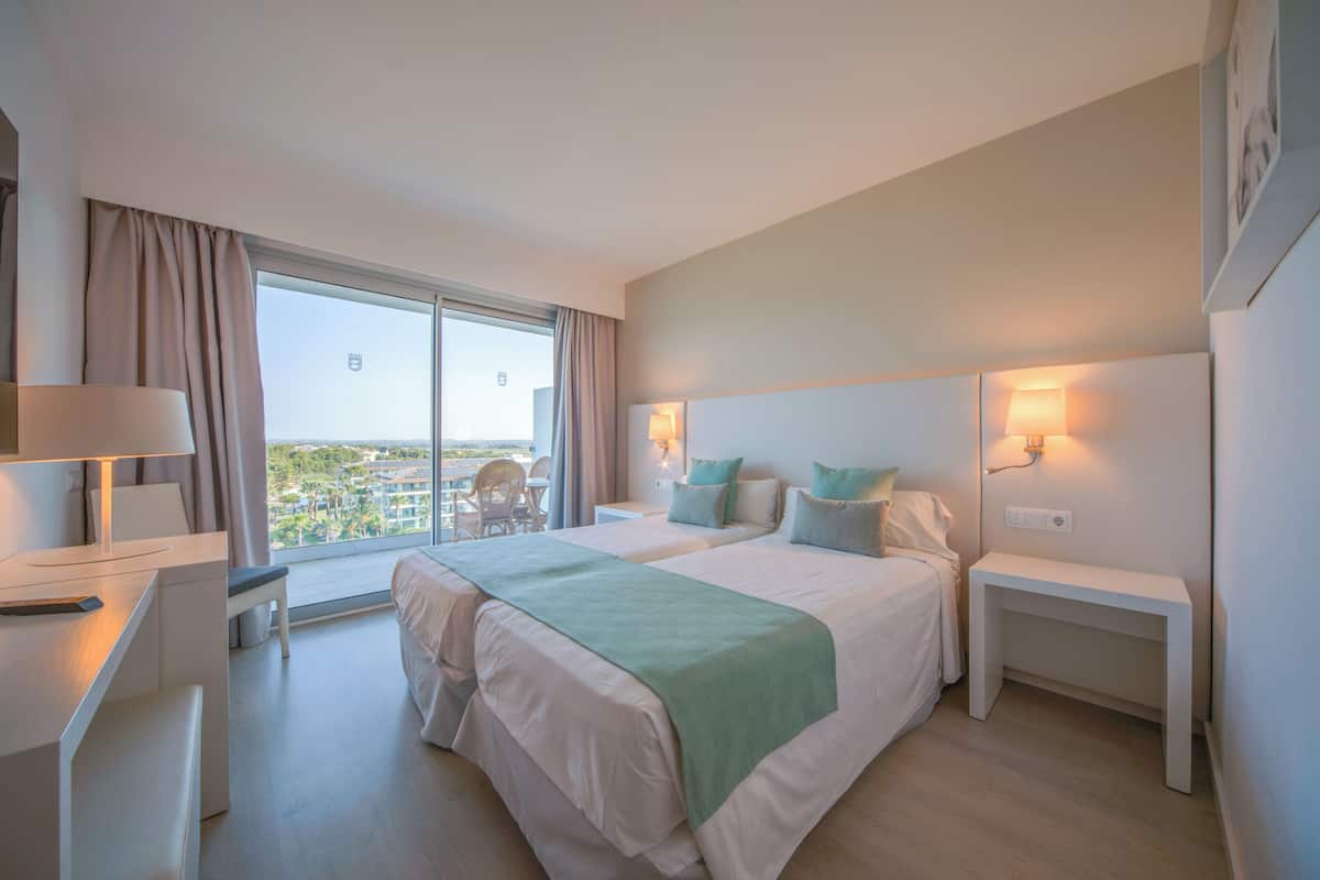 A hotel room with two beds, a desk, a chair, and a view of the city.