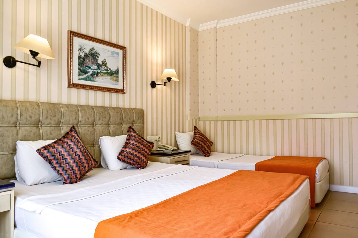 A hotel room with two beds, striped wallpaper, and wall-mounted lamps.