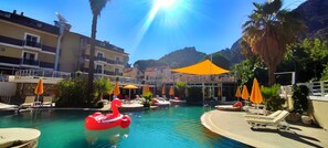 Ein Schwimmbecken mit Liegestühlen und Sonnenschirmen, umgeben von Gebäuden und Palmen.