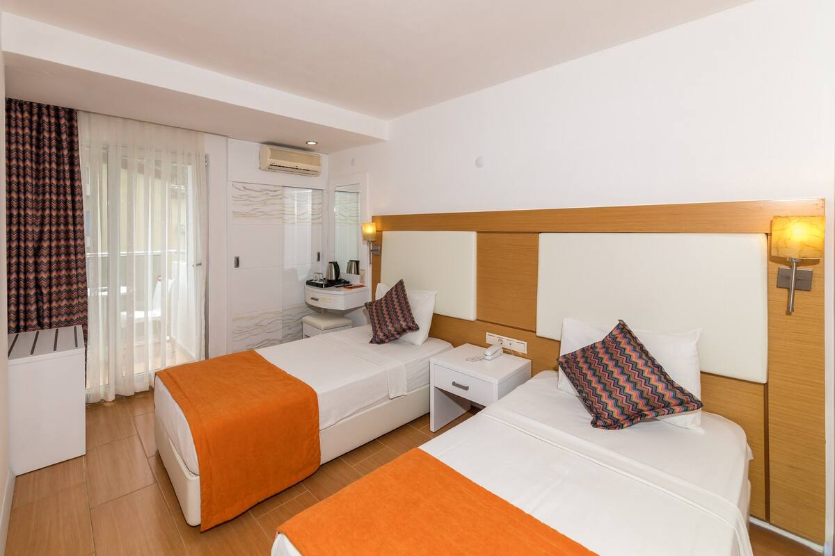 A hotel room with two beds, a TV, a bathroom with a mirror, and a bedside table with a lamp.