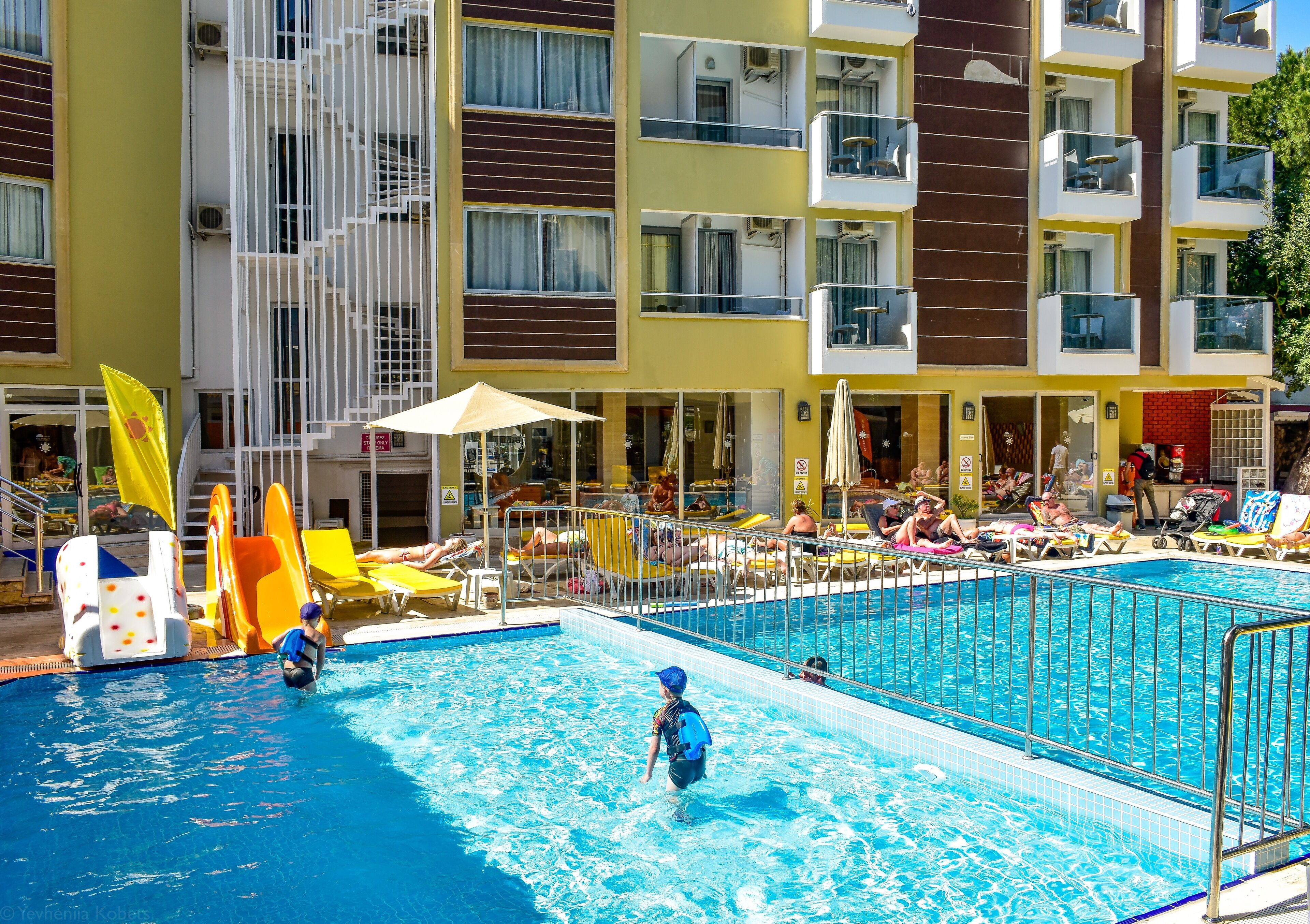 A swimming pool area with a water slide, sun loungers, and a building with balconies.