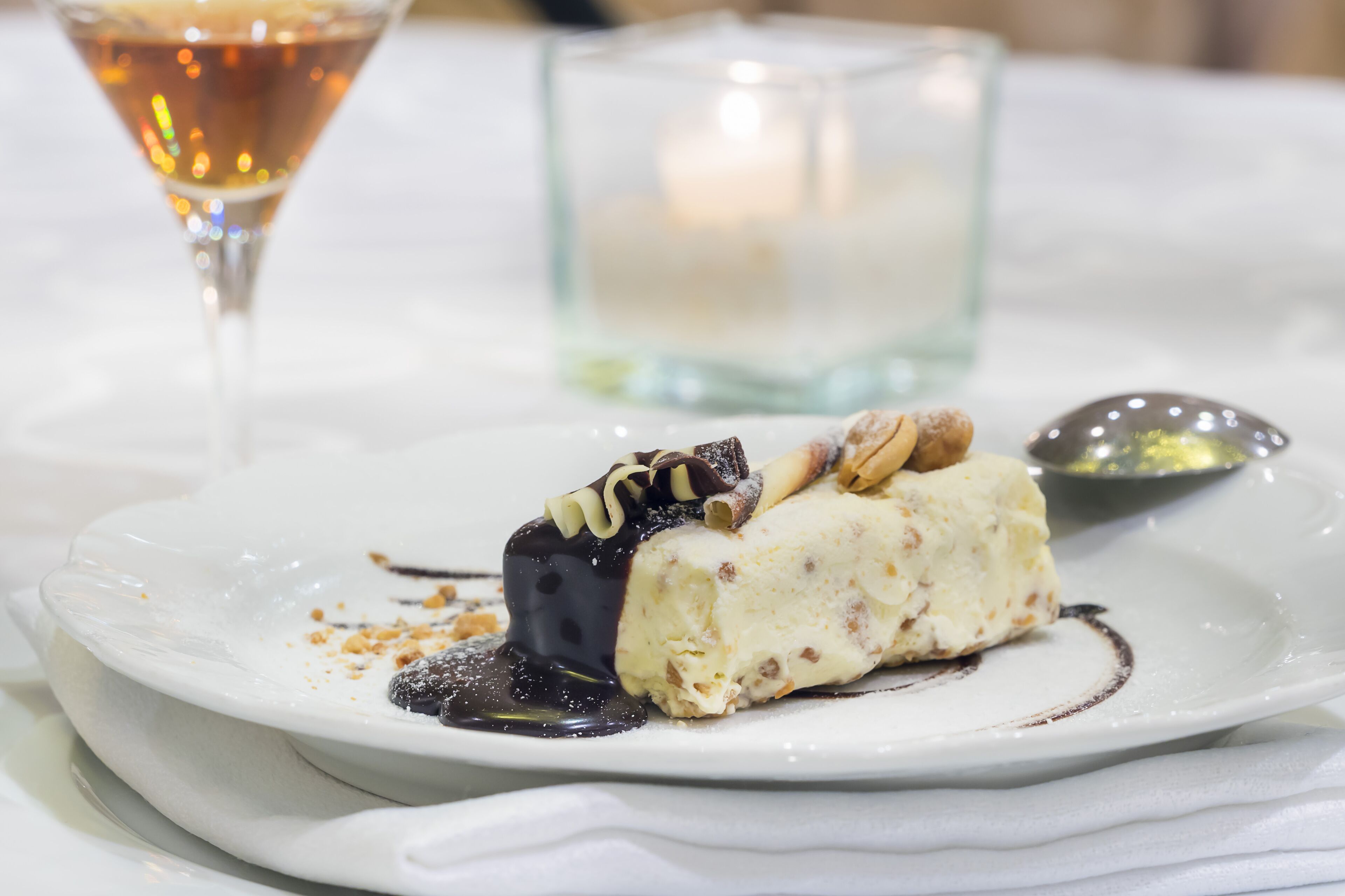 A dessert on a white plate with a glass of a light-colored beverage and a candle in the background.