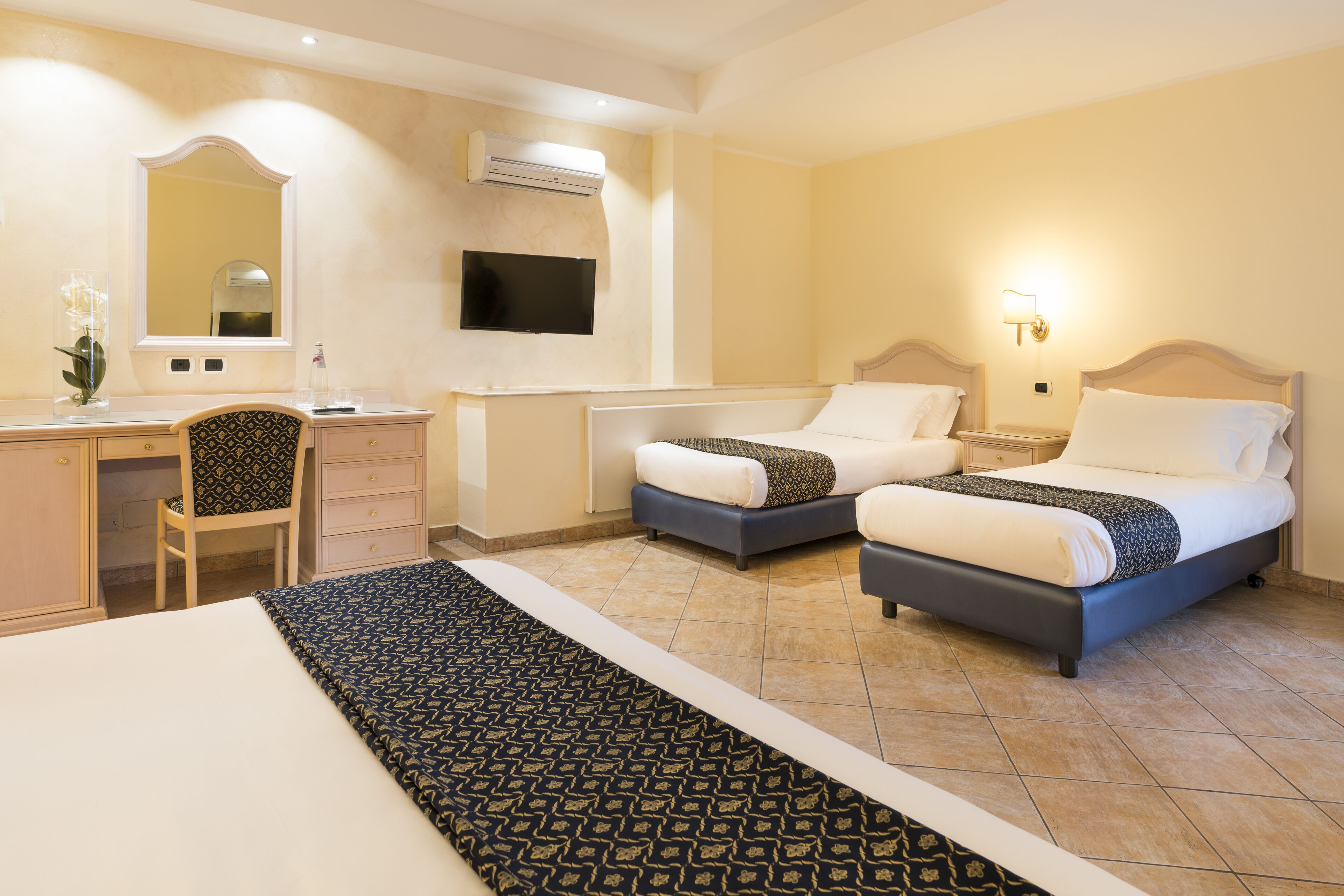 Habitación de hotel con dos camas, un escritorio, una silla, un televisor y un espejo.