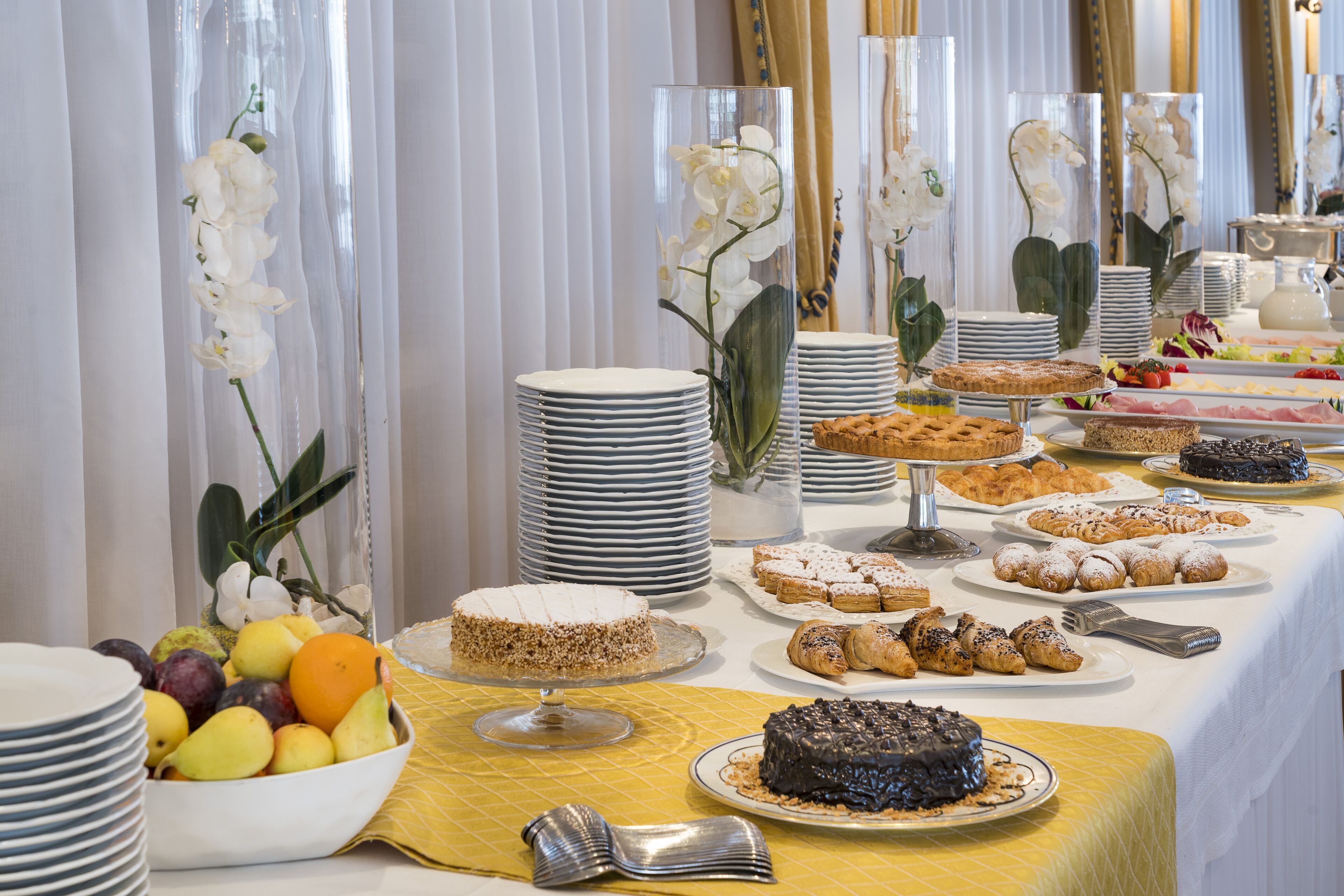 A buffet table with various desserts and fruits, surrounded by white orchid flowers in glass vases.