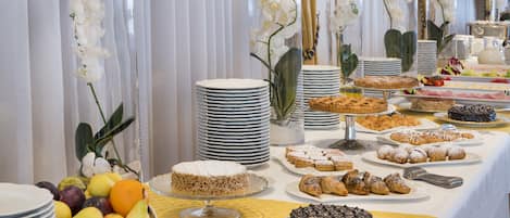 A buffet table with various desserts and fruits, surrounded by white orchid flowers in glass vases.