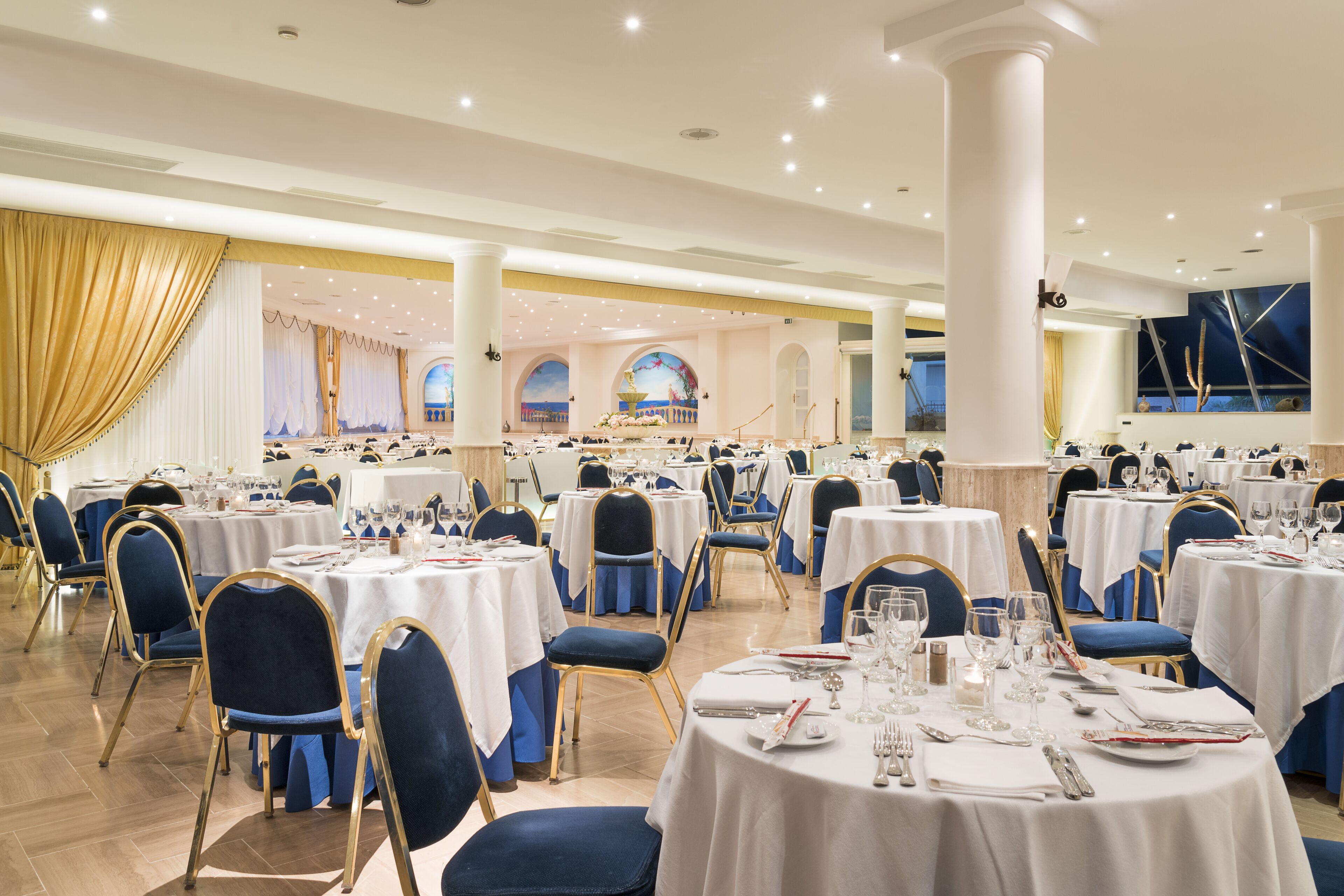 A banquet hall with round tables, blue chairs, and white tablecloths.