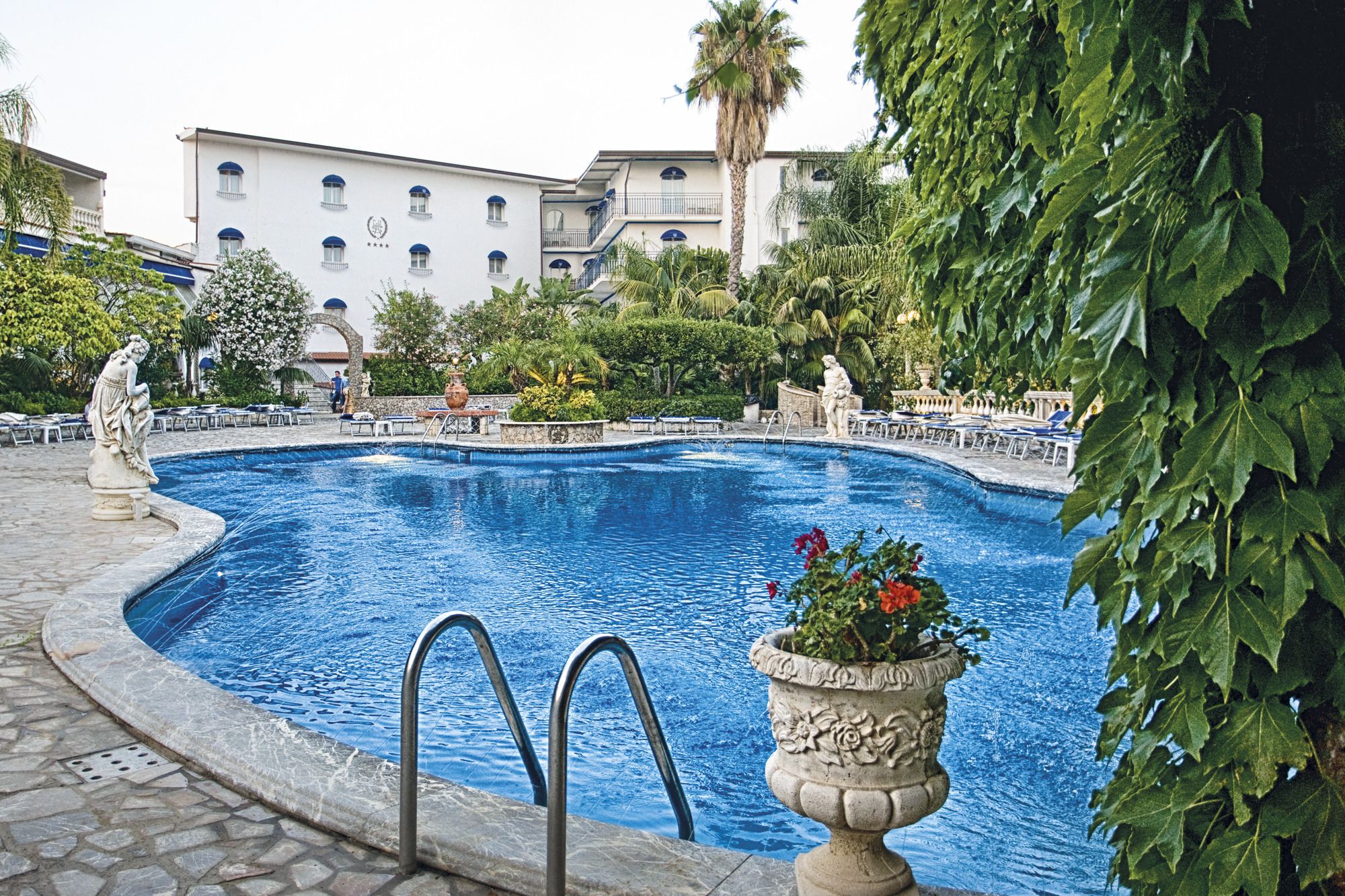 A swimming pool with a stone border, a statue, and a building in the background.
