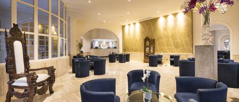 A spacious lobby with a classic wooden chair, modern seating, and a reception area in the background.
