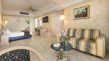 A hotel room with a bed, a sofa, a desk, a chair, a coffee table, and a painting on the wall.