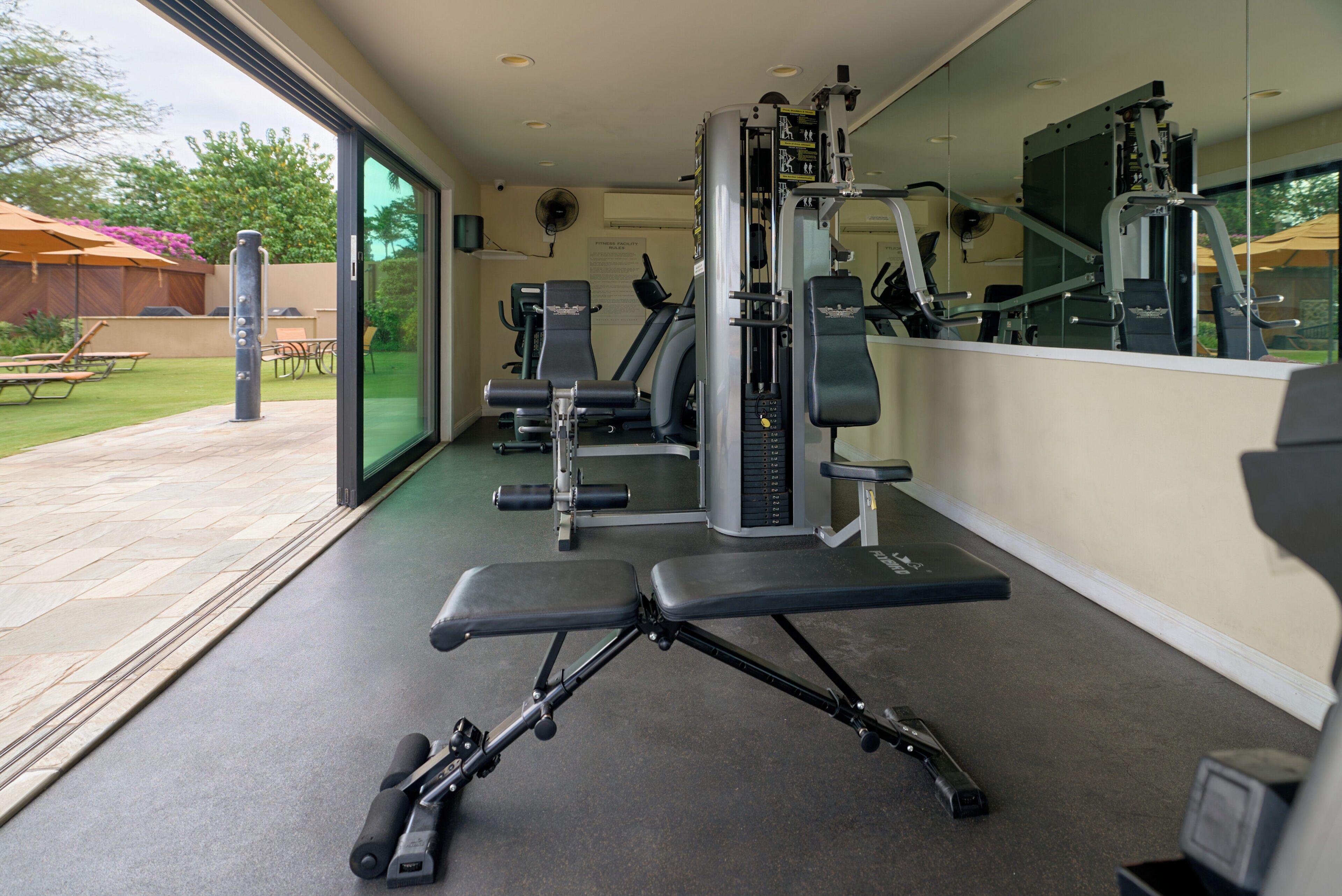 Un gimnasio con equipo de ejercicio, una banca y un patio con mobiliario exterior.