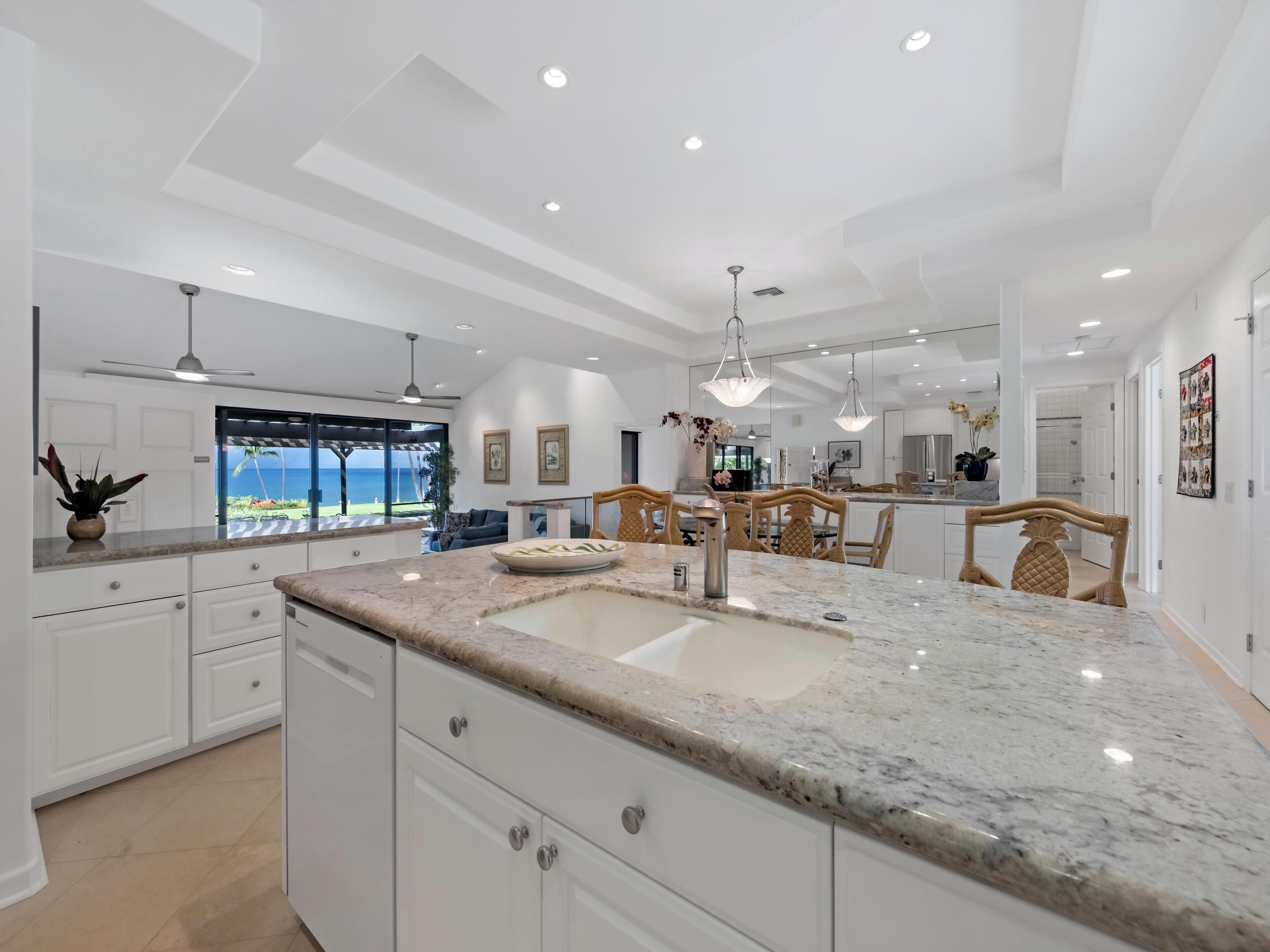 A modern kitchen with a large island, white cabinetry, and a view of the ocean.