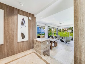 A modern interior with a marble reception desk, a large framed artwork, and a view of a lush garden and ocean. - Wailea Elua- CoralTree Residence Collection (Kihei)