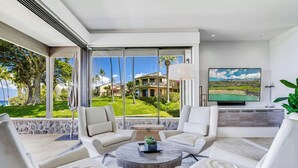A modern living room with a large window, a flat-screen TV, and a round coffee table. - Wailea Elua- CoralTree Residence Collection (Kihei)