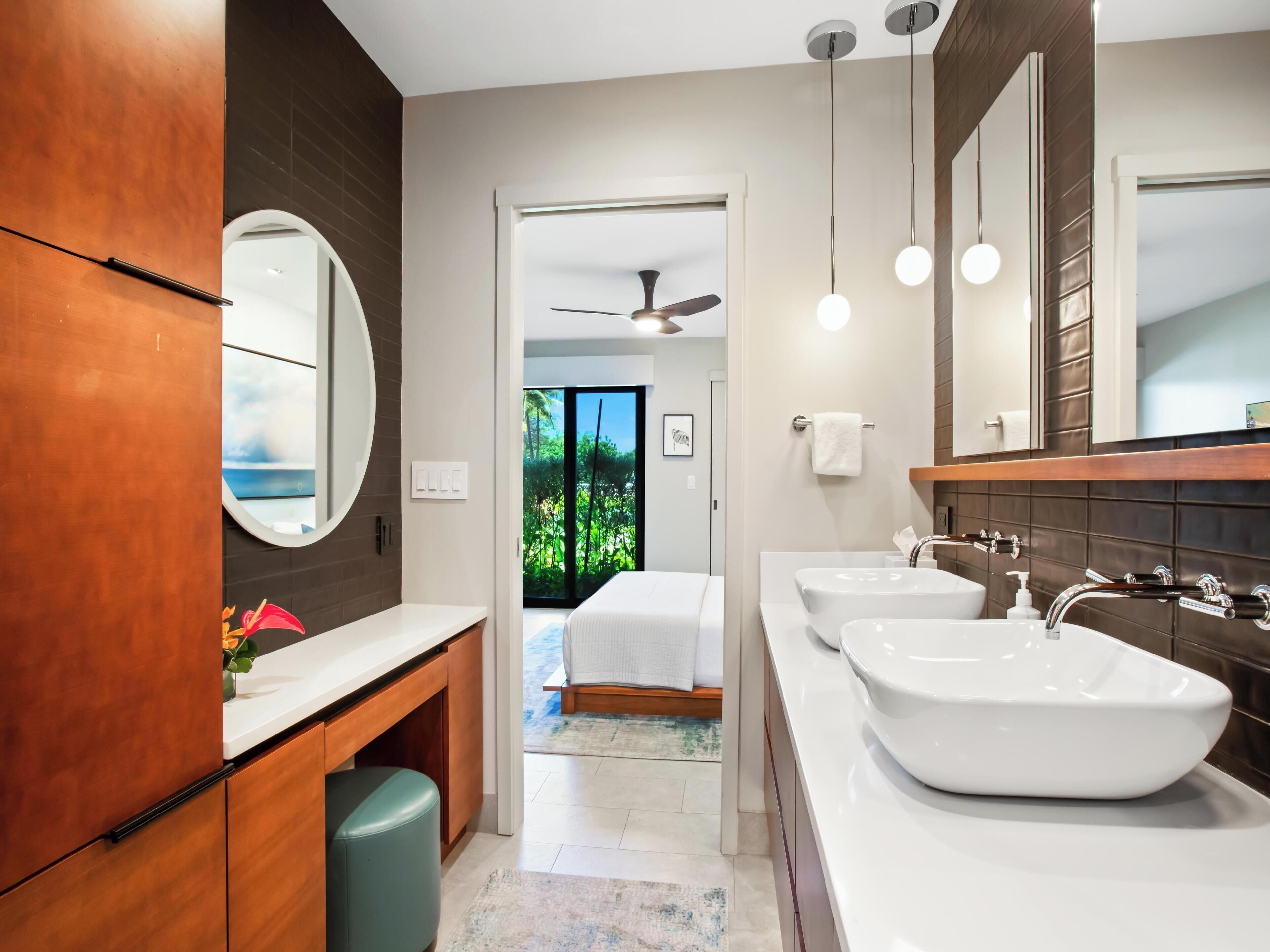 A modern bathroom with two sinks, a large mirror, and a view of a bedroom through an open door.