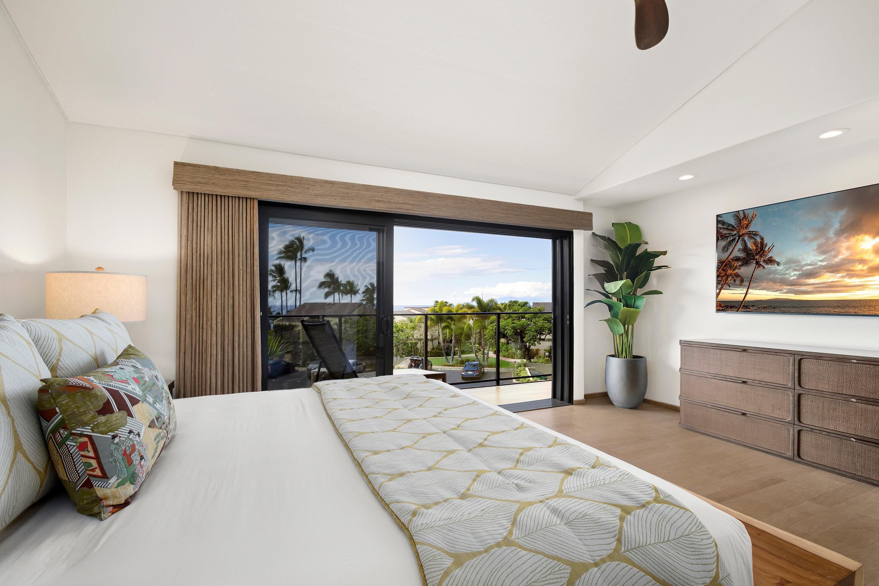 A modern bedroom with a large bed, a balcony with a view, a potted plant, and a painting on the wall.
