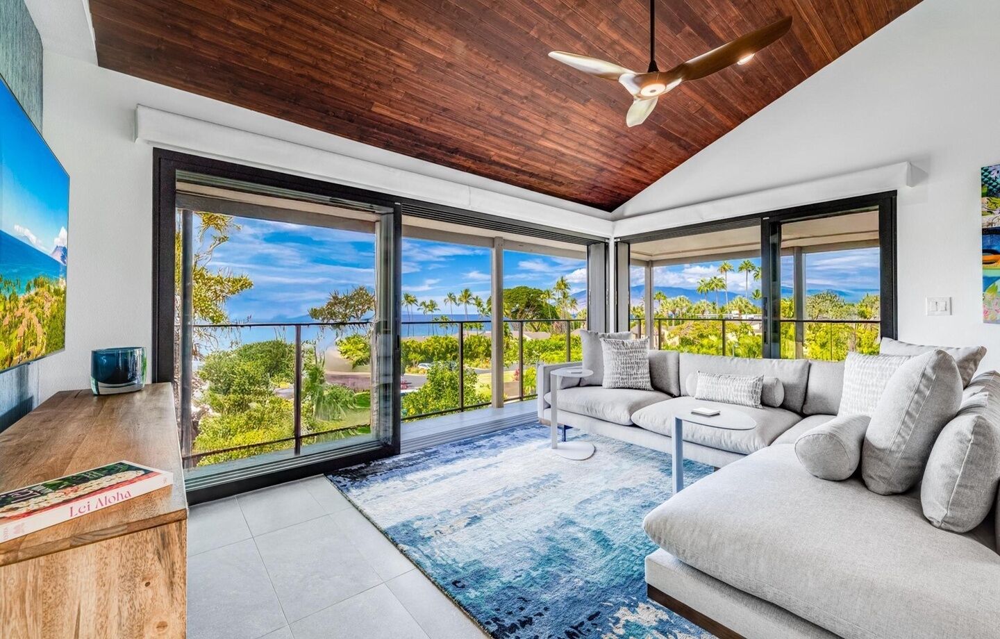 A modern living room with a large sofa, a coffee table, and a view of a lush landscape through expansive glass doors.