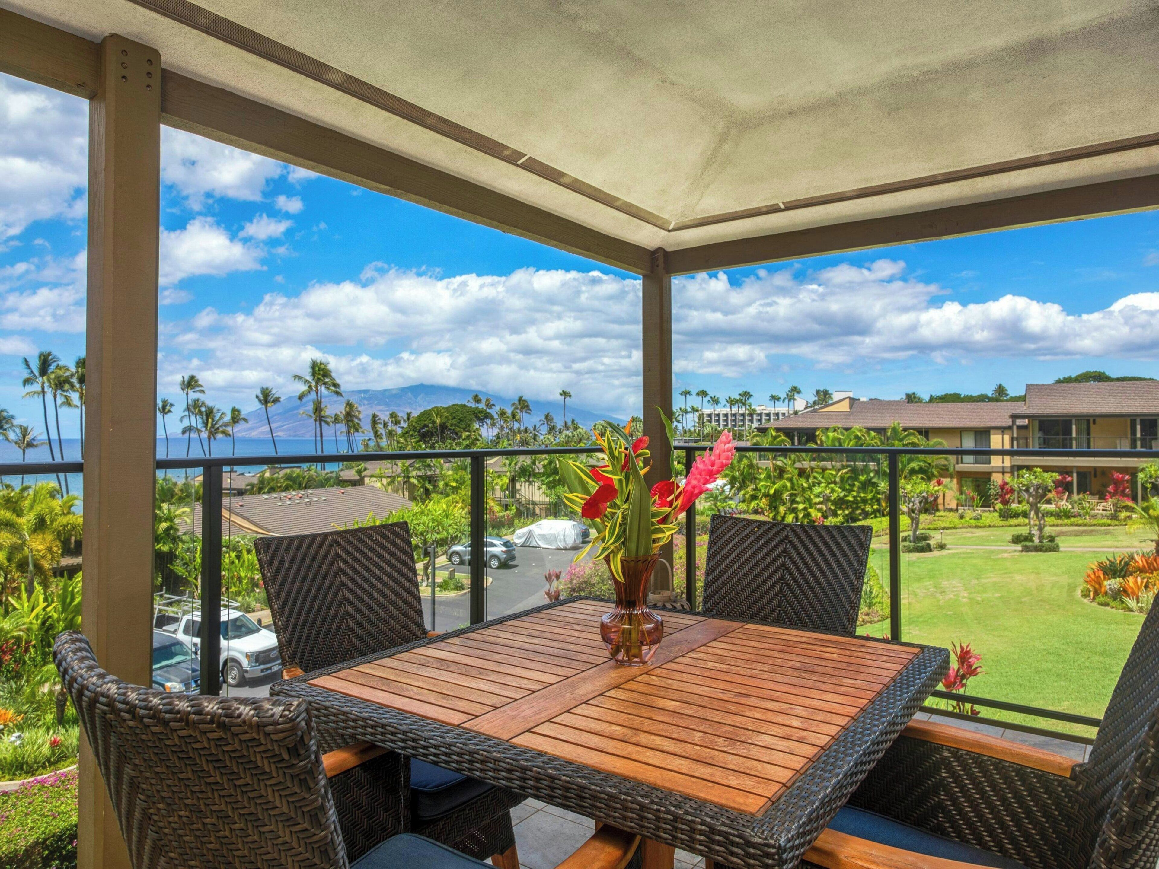 A covered outdoor seating area with a table and chairs, overlooking a landscaped garden and a view of the ocean.