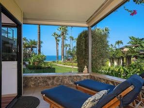 A balcony with two lounge chairs, a stone wall, and a view of the ocean and palm trees. - Wailea Elua- CoralTree Residence Collection (Kihei)