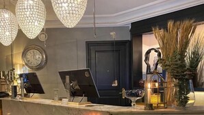 Un comptoir d’accueil en marbre agrémenté d’une horloge, de luminaires décoratifs et d’un vase contenant des plantes séchées.