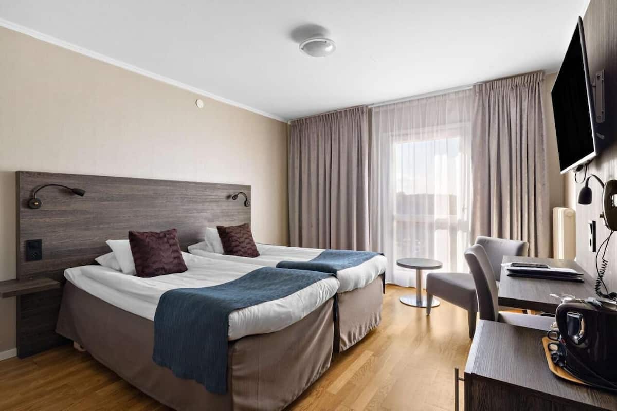 A hotel room with a large bed, a desk with a chair, a television, and a window with curtains.