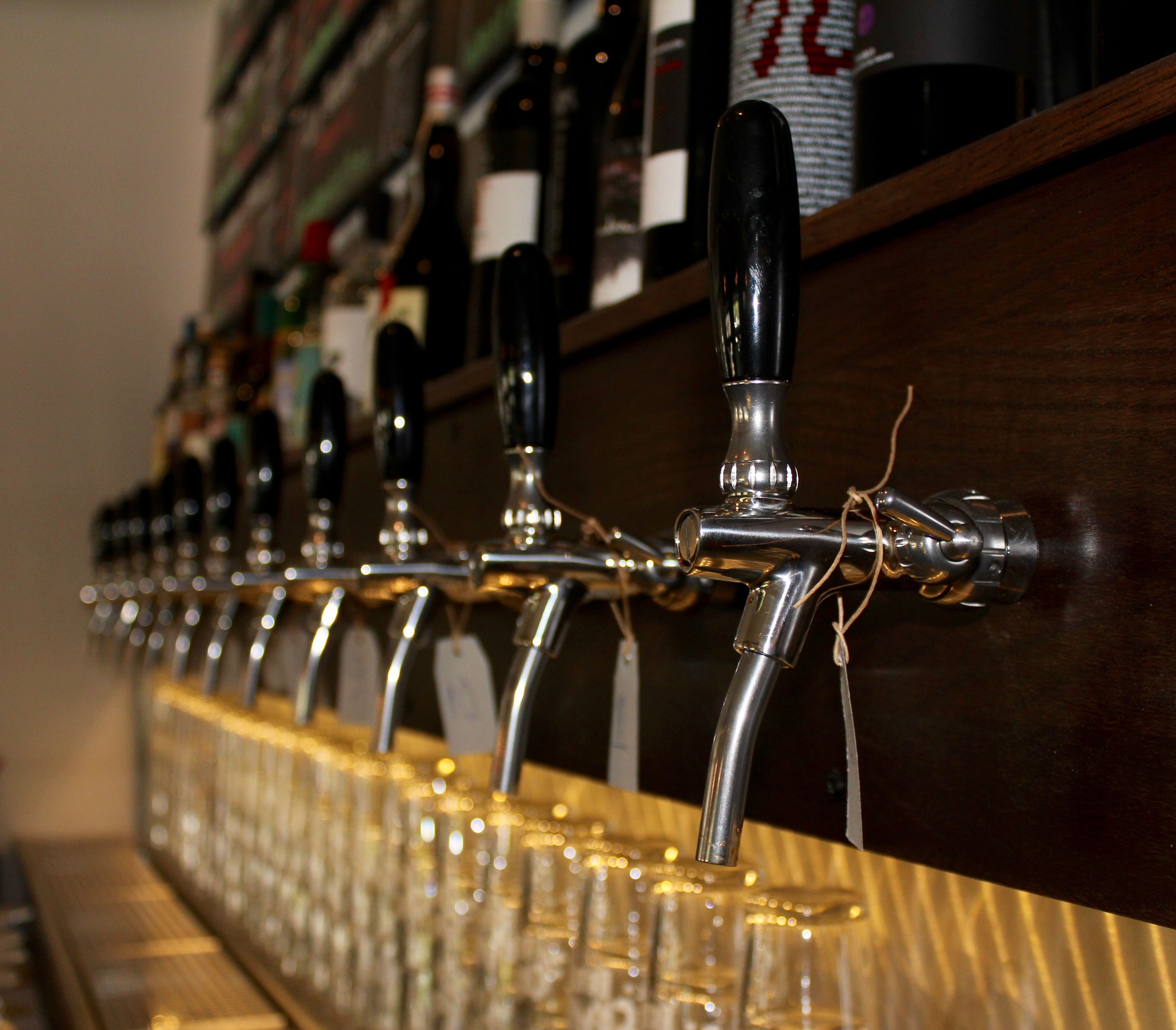 A row of beer taps with labels, mounted on a wooden bar counter.