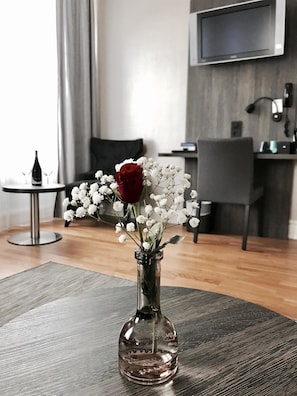 A modern room with a dining table, a vase with flowers, and a flat-screen TV mounted on the wall.