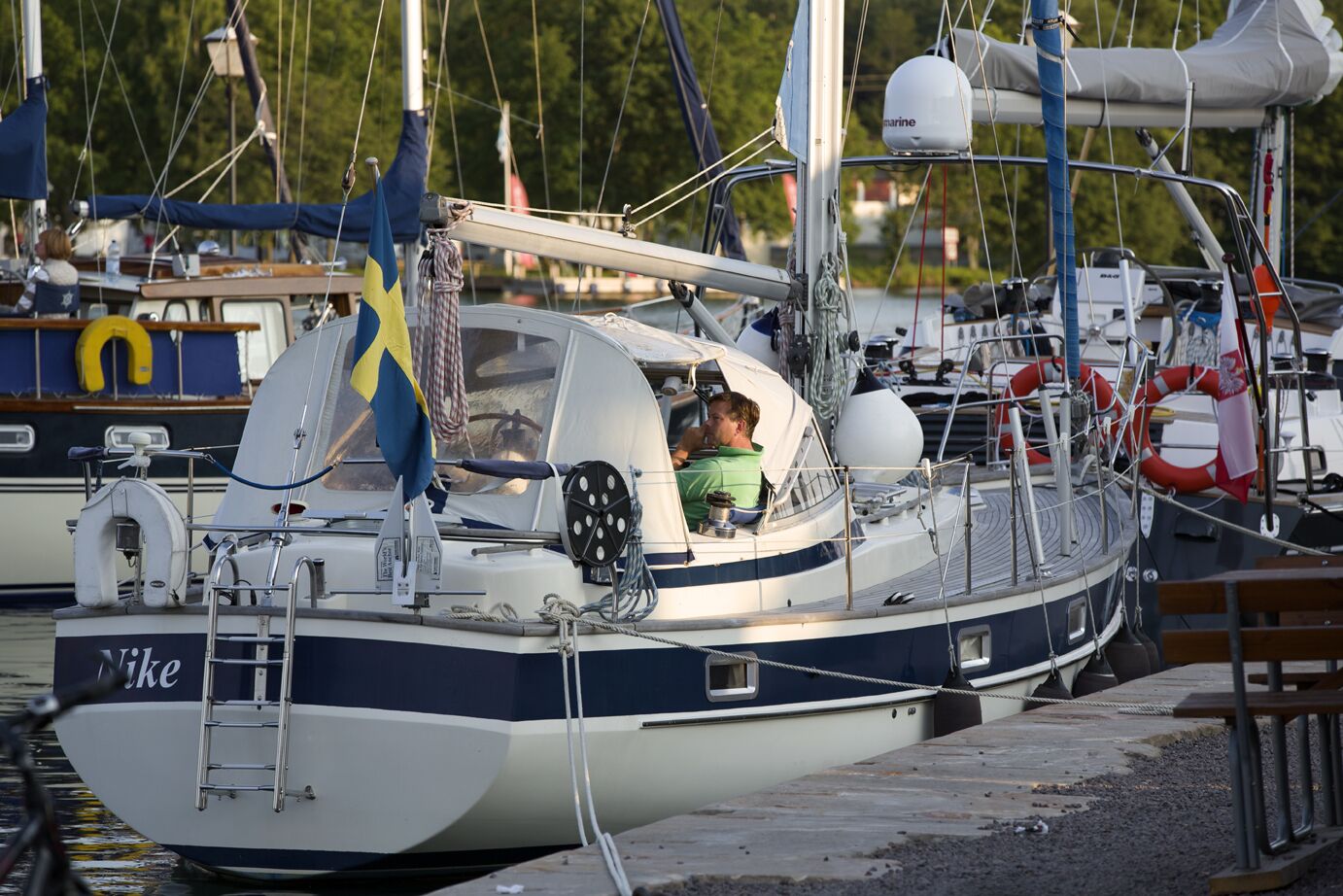 Ein Boot liegt in einer Marina festgemacht, mit einer Person an Bord, Rettungsringen und einer Flagge.