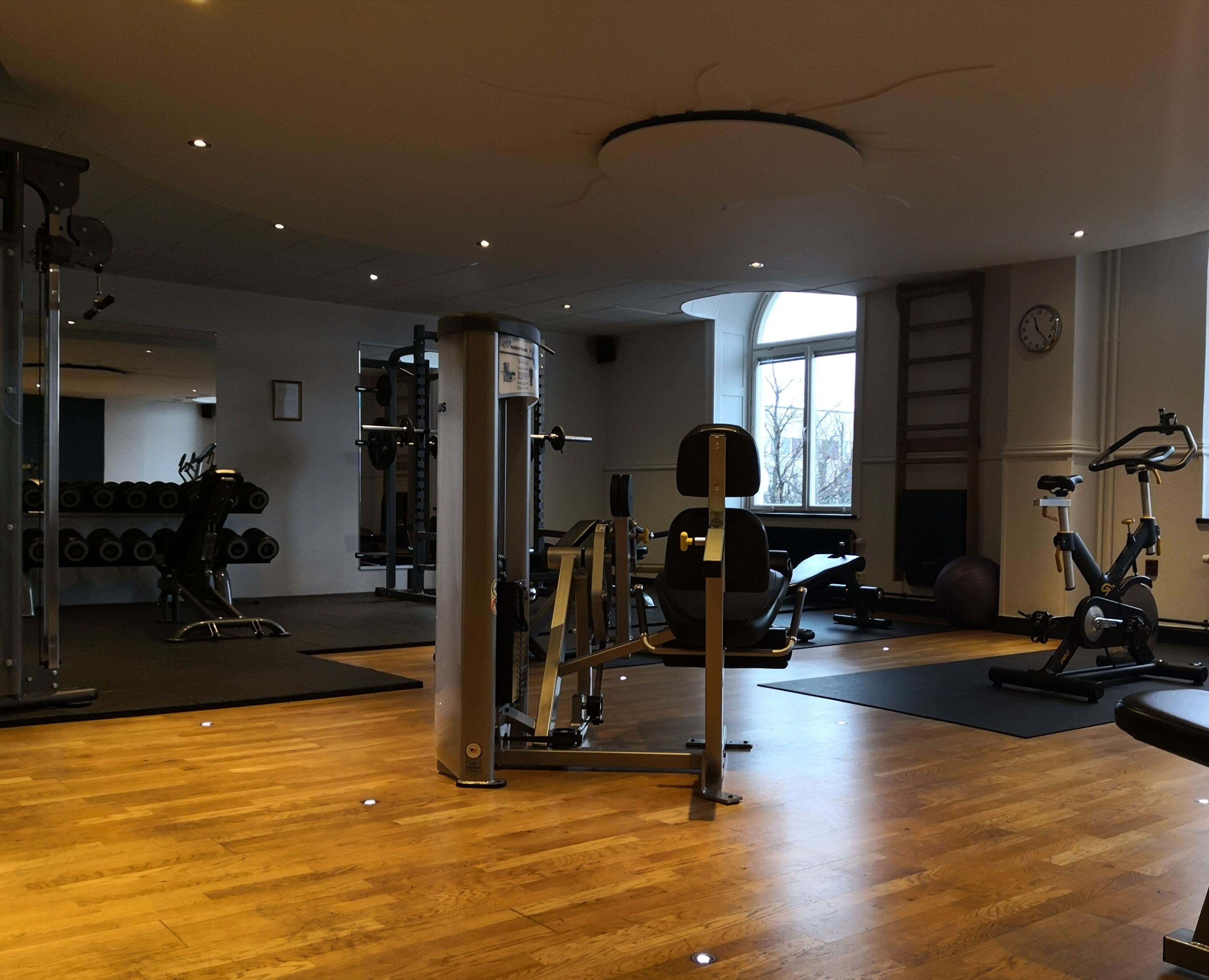 A gym with exercise equipment, a window, and a clock on the wall.