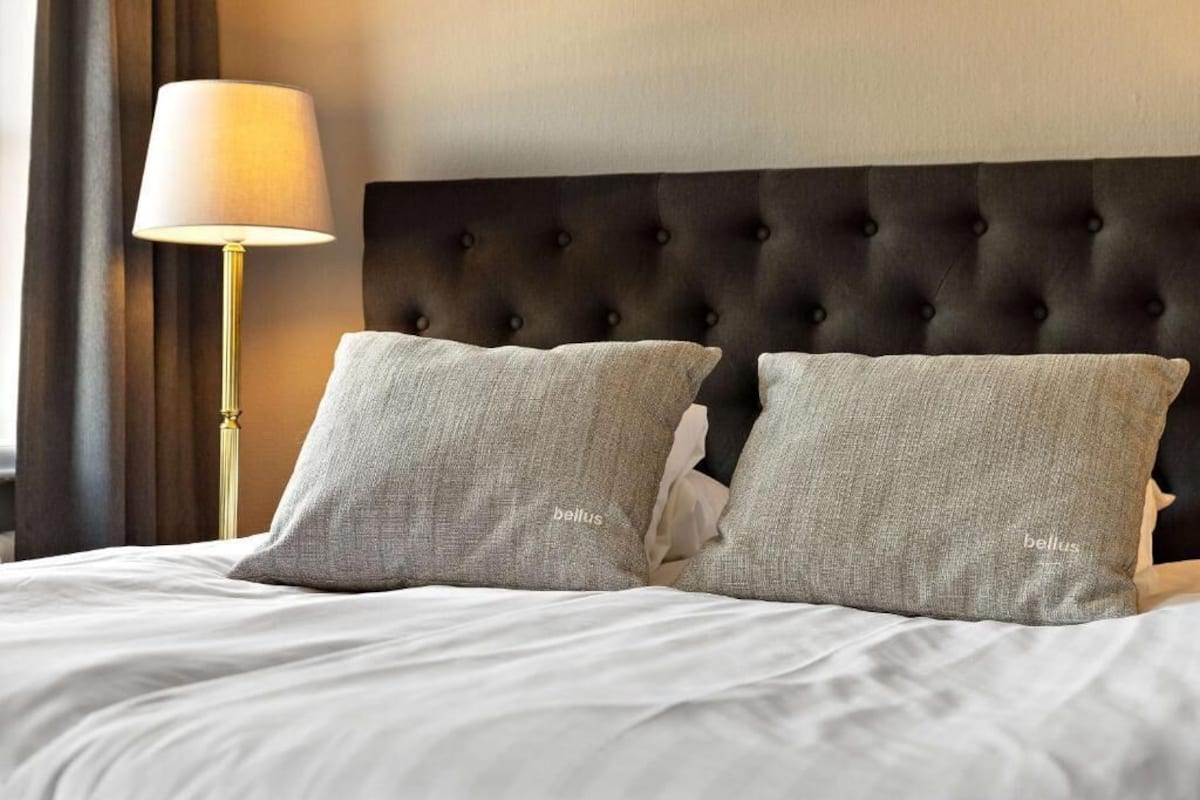 A hotel room with a tufted headboard, two pillows, a lamp, and a bed.