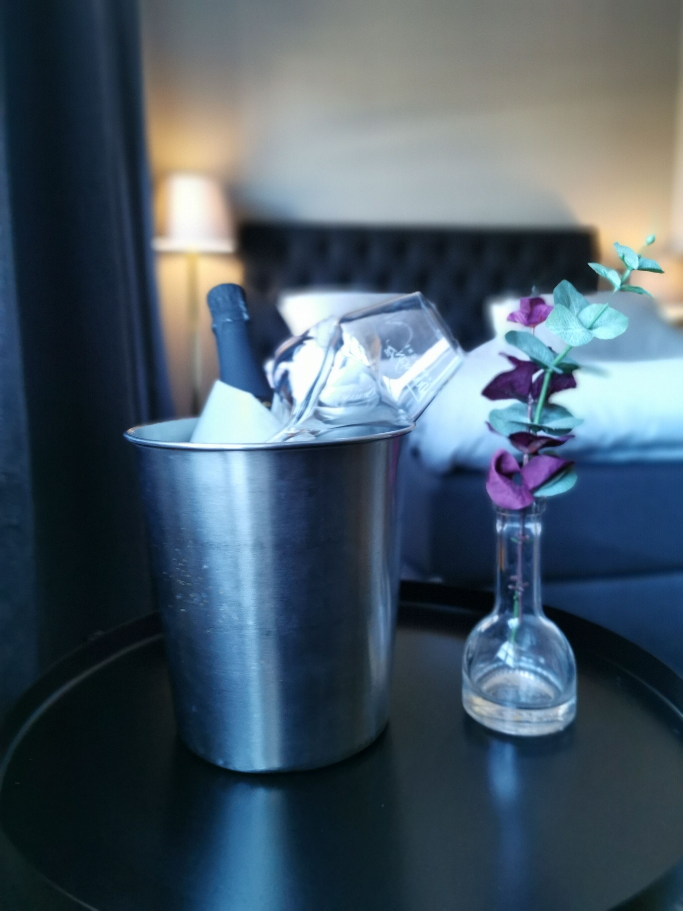 A metallic cup with ice cubes and a small glass vase with a purple flower on a black table.