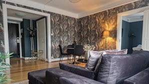 Un salon moderne avec un canapé aux couleurs sombres, une table à manger avec des chaises et un papier peint à motifs.
