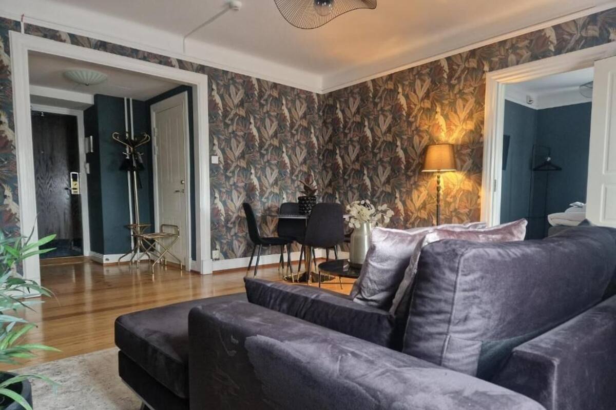 A modern living room with a dark-colored sofa, a dining table with chairs, and a patterned wallpaper.