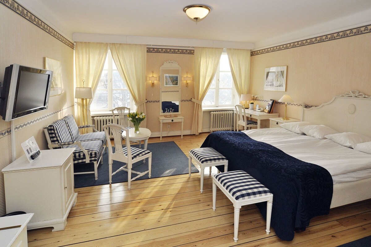 Una habitación de hotel con cama, escritorio, silla, televisión y ventana con cortinas.