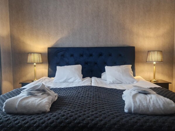 Habitación de hotel con una cama grande, dos lámparas de noche y un cabecero azul oscuro.