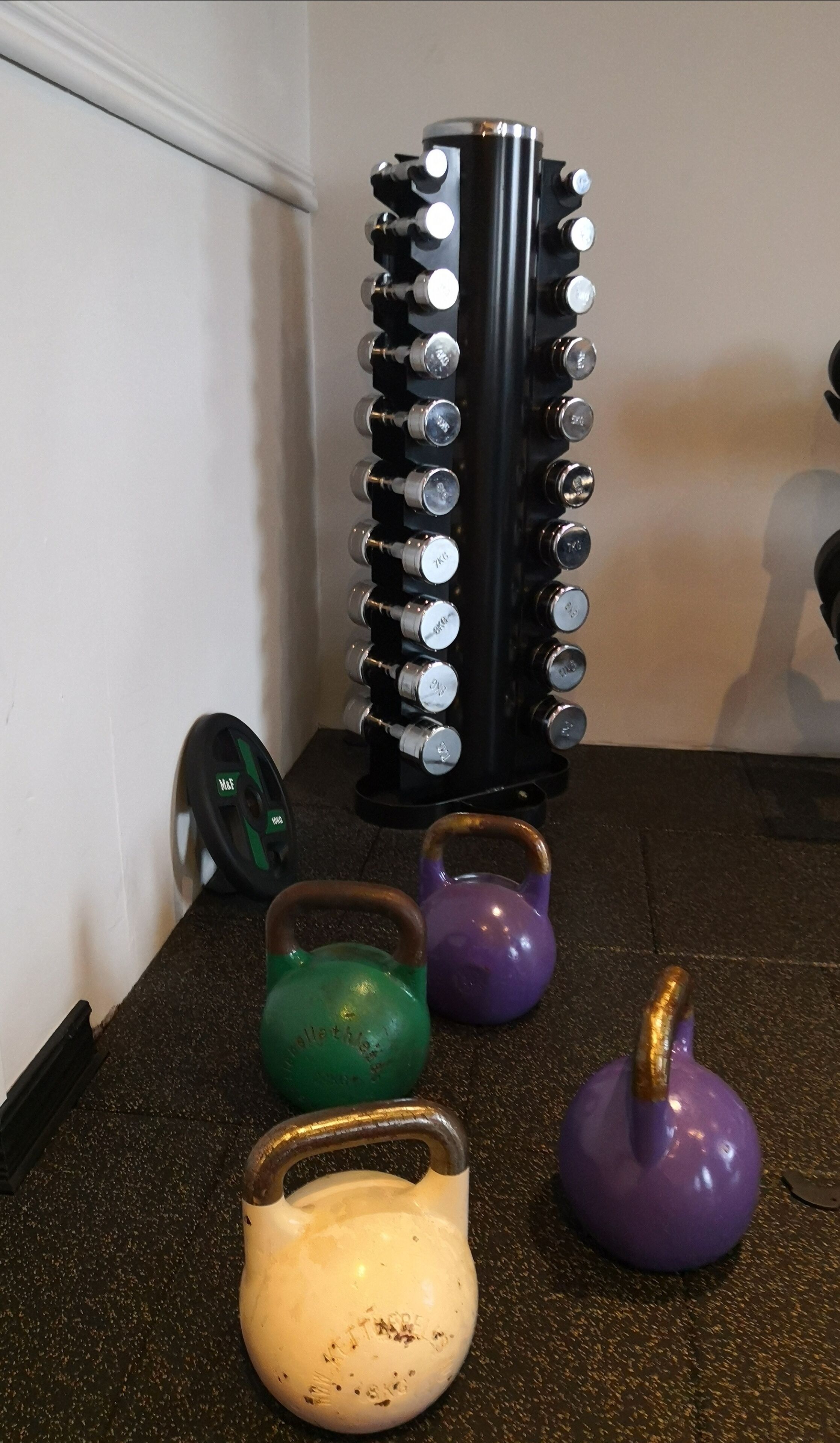 A home gym setup with a weight stack, kettlebells, and a kettlebell holder.