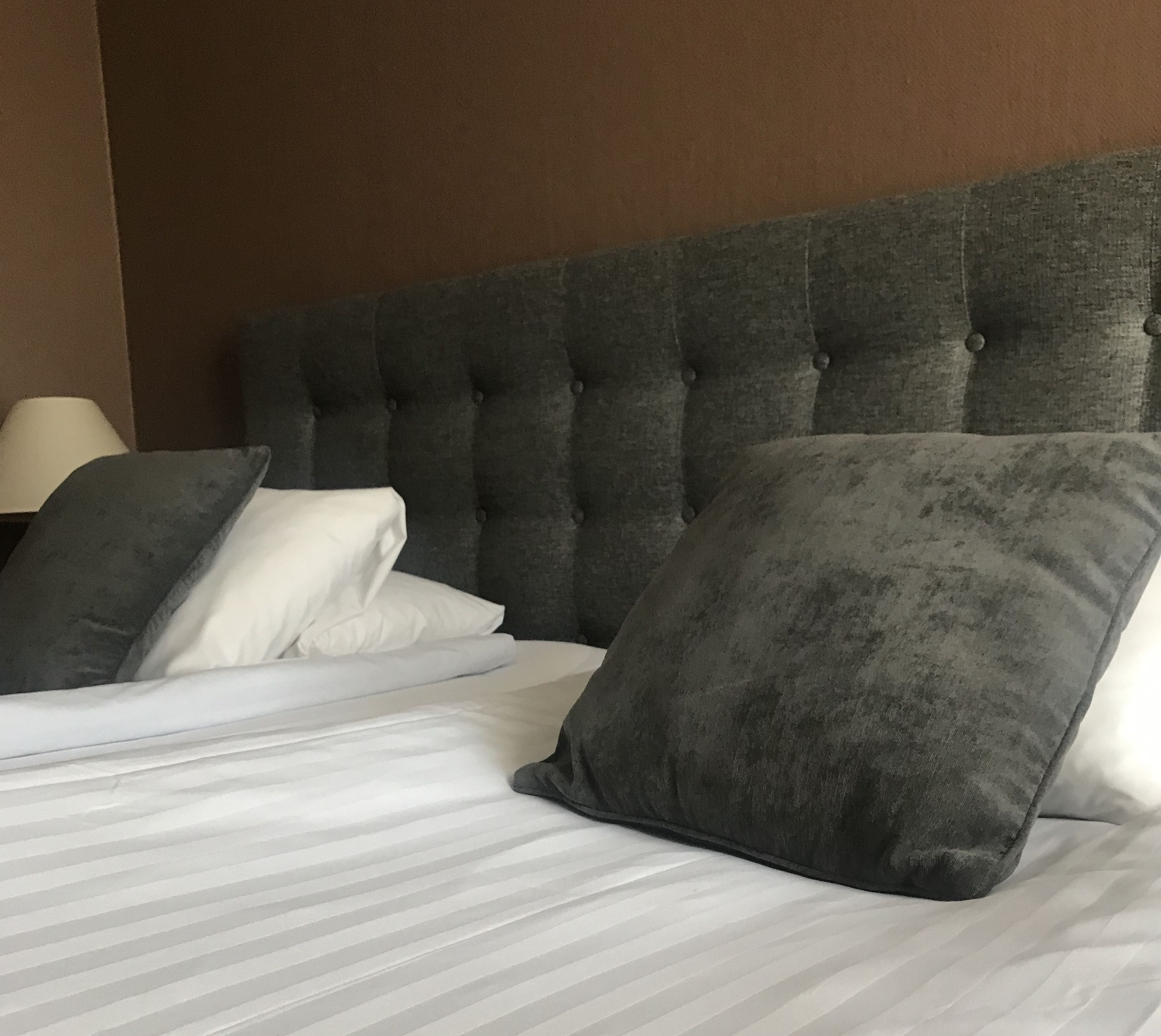 A bed with a tufted headboard, white linens, and two dark gray pillows.