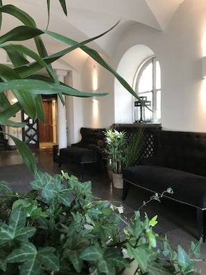 Ein modernes Interieur mit einem schwarzen Sofa, Topfpflanzen und einer Treppe, die zu einer Holztür führt.