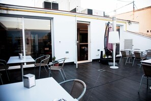 An outdoor patio area with tables and chairs, a white building with a glass door, and a lamp post. - Universal Hotel (Granada)