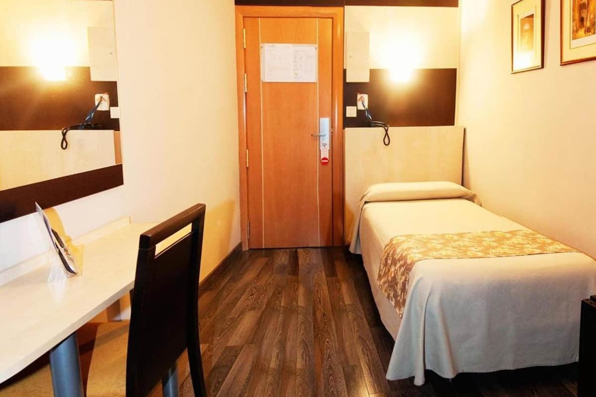 A small hotel room with a desk, chair, two single beds, and a door with a notice.