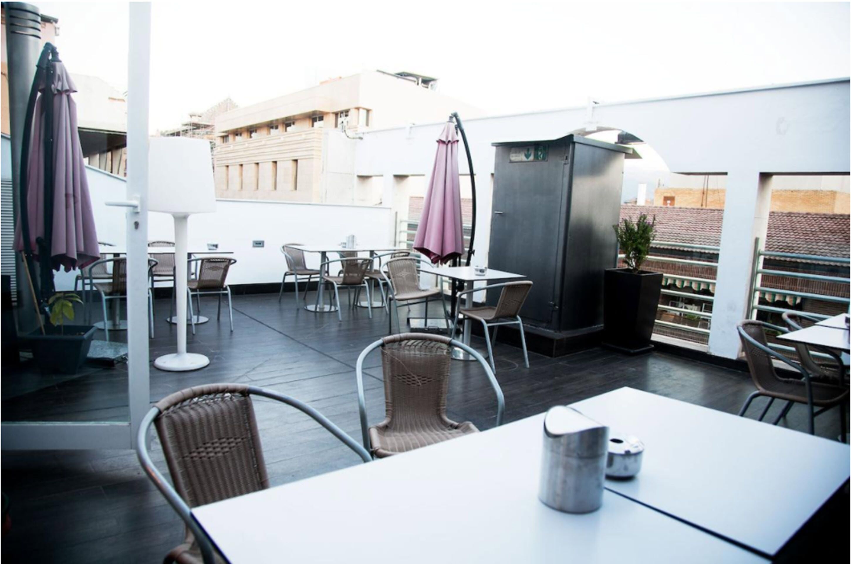 An outdoor patio area with tables and chairs, umbrellas, and a potted plant.