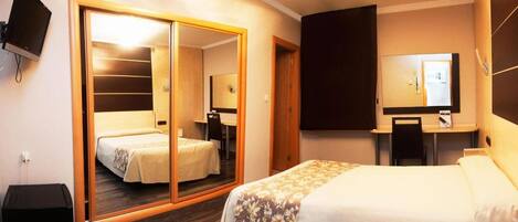 A hotel room with a large mirror, a bed, a desk with a chair, and a television mounted on the wall.
