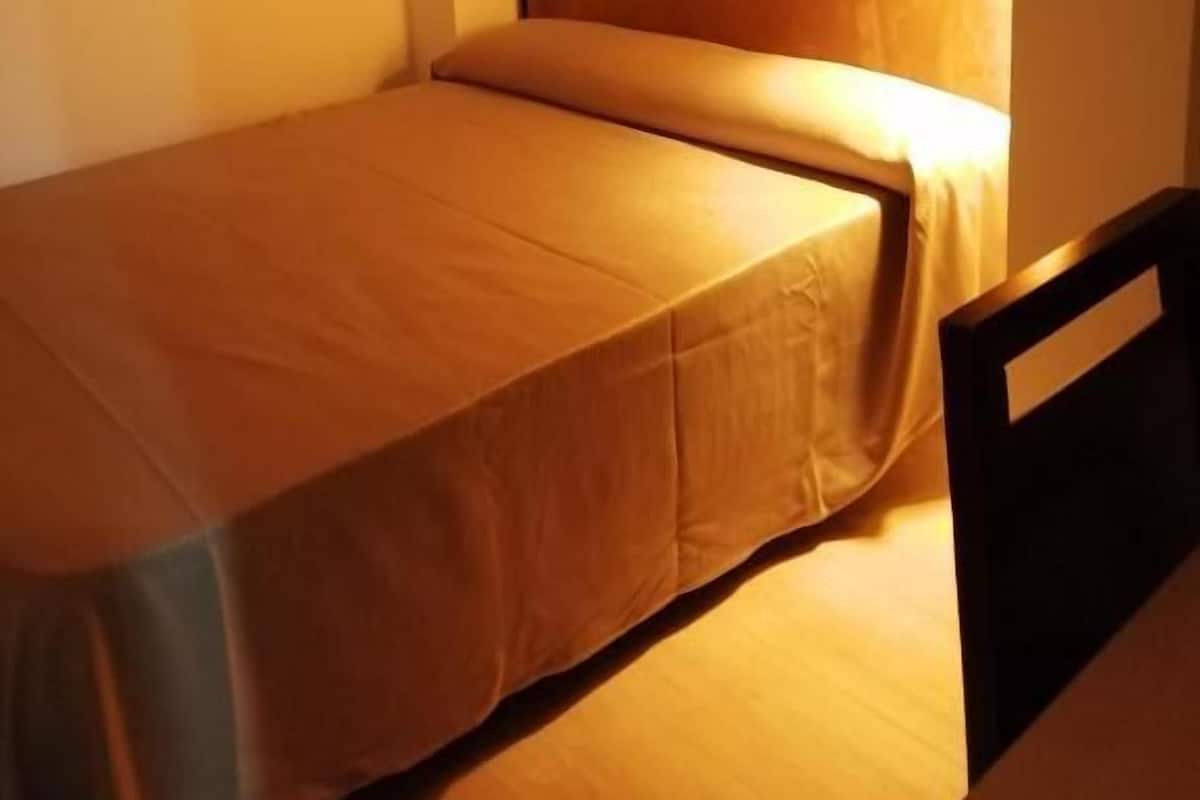 A small, single-bed room with a wooden headboard and a bedside table.