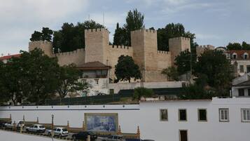Um castelo de pedra histórico com duas torres imponentes, rodeado por árvores e edifícios modernos.