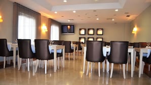 A dining area with tables and chairs, a television mounted on the wall, and framed pictures on the wall.