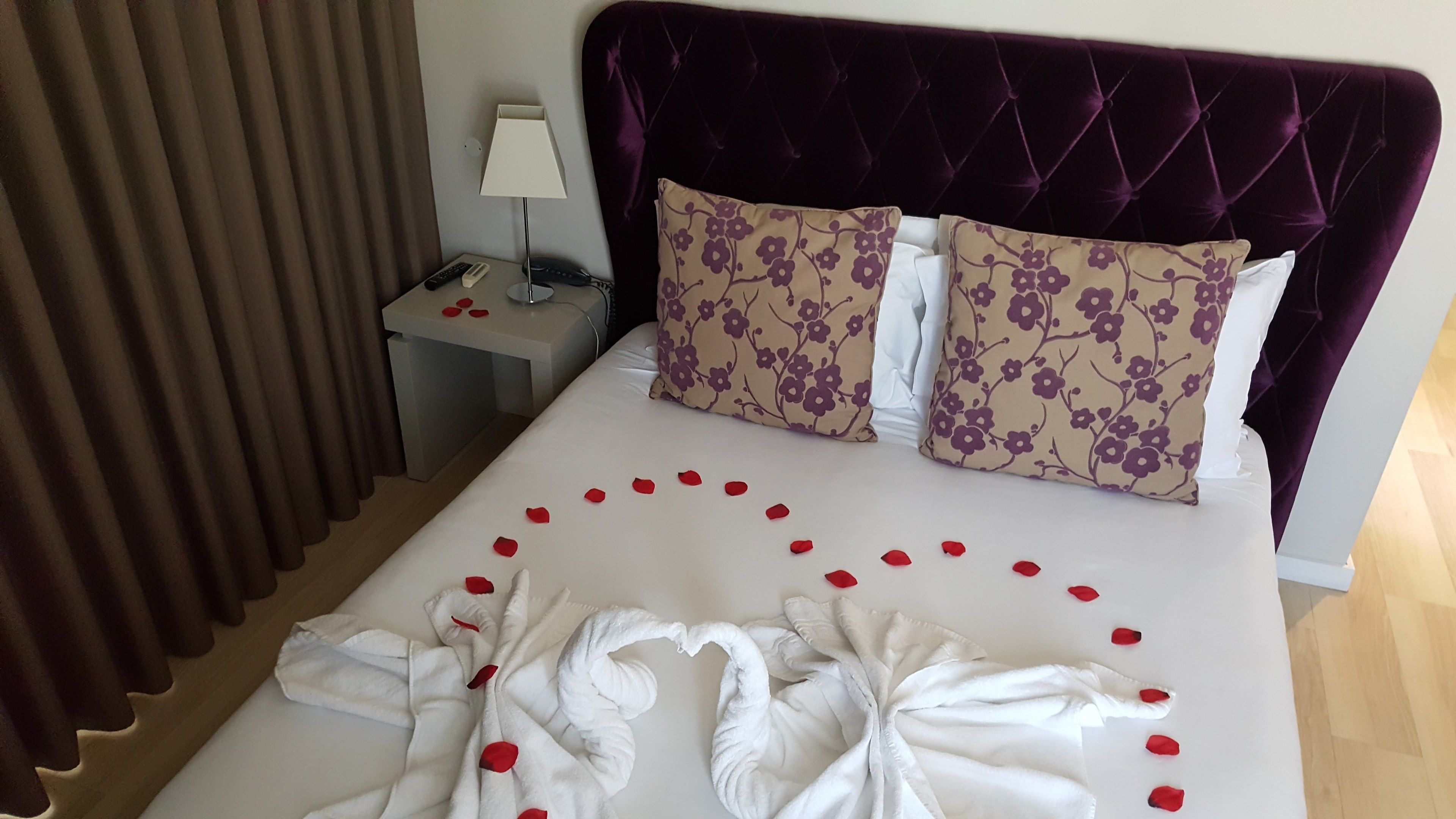 A hotel room with a bed, a nightstand, a lamp, and a window with curtains.
