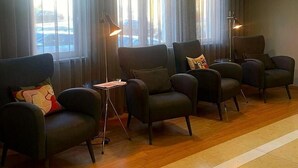 A hotel lobby with a row of dark leather armchairs, a floor lamp, and a large window with curtains.