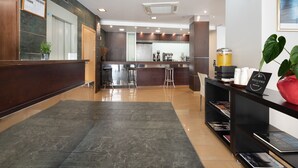A modern hotel lobby with a reception desk, a coffee bar, and a seating area.