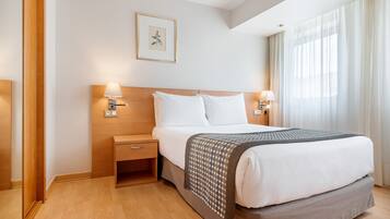 A hotel room with a large bed, wooden headboard, bedside tables with lamps, a framed picture on the wall, and a window with curtains.
